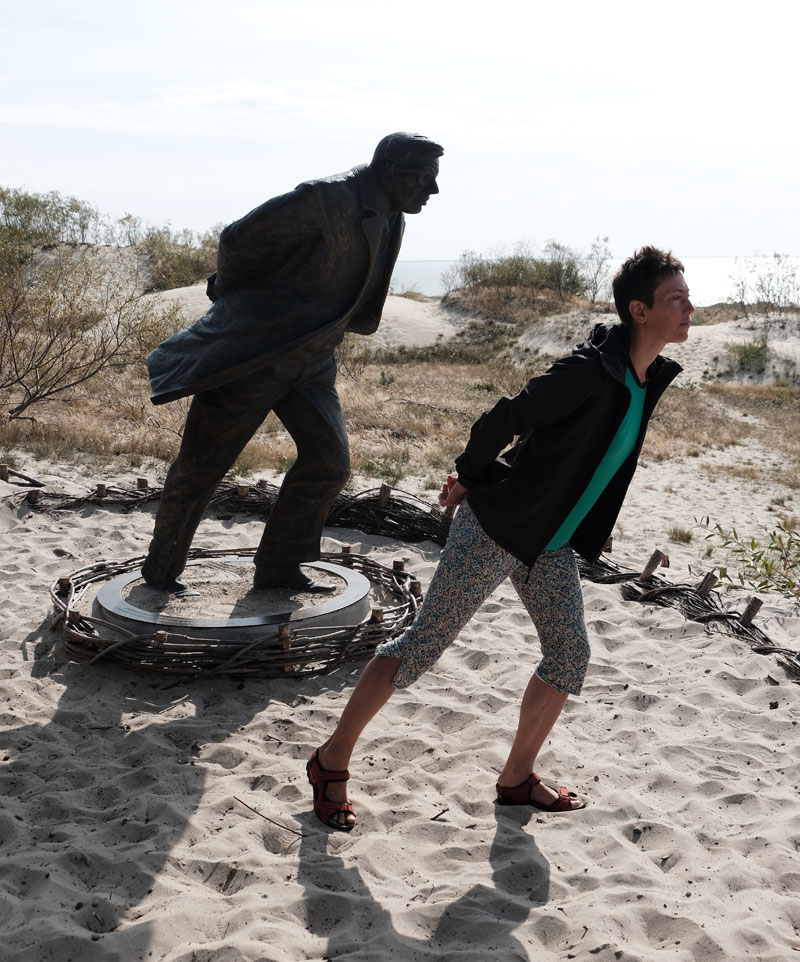 Skulptur aus Bronze und eine Persone lehnen sich gegen den Wind